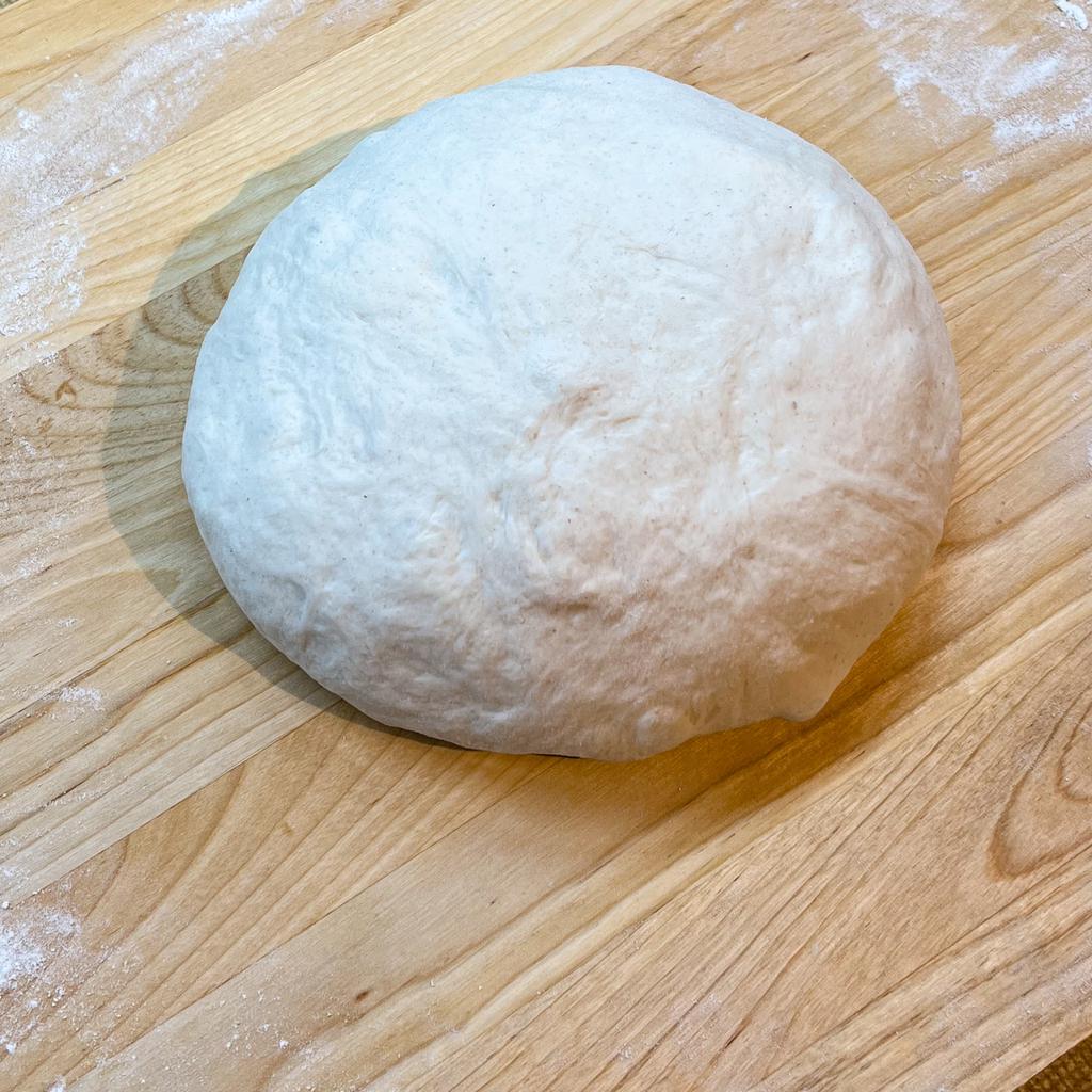 Sourdough ball on a breadboard, gently kneaded after the third hour of rising.