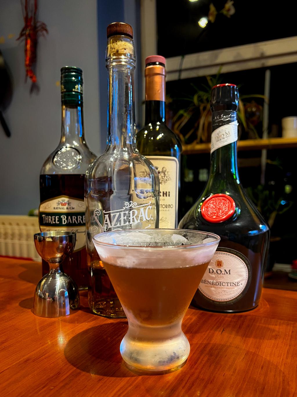 A cocktail and liquor bottles on the table in front of a window at night.