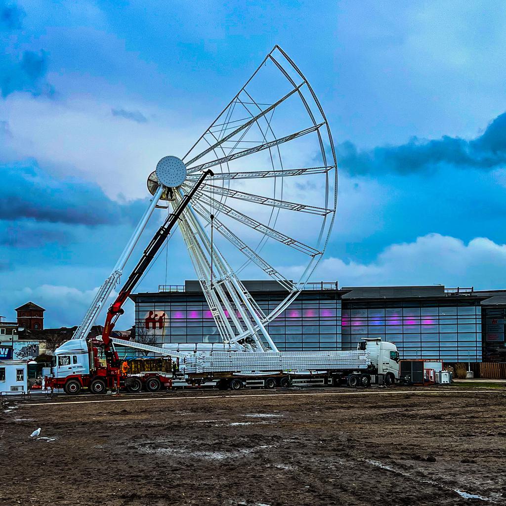 A Ferris wheel in the process of being deconstructed such that a little more than a quarter of the wheel remains.