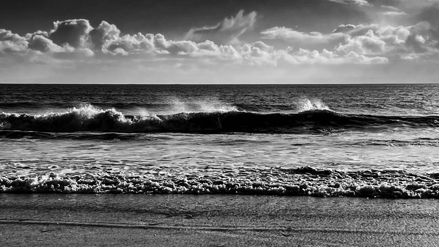 Black and white photo of a (small) windswept wave breaking just off shore