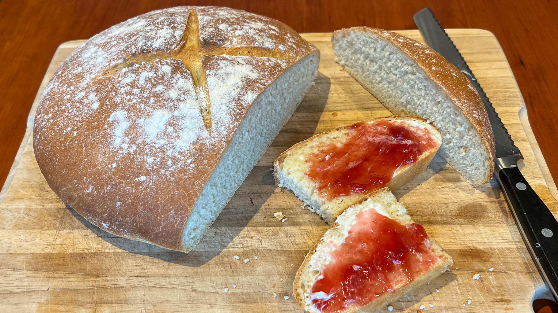 A plain, white loaf of bread sliced open and featuring a couple of slices with butter and jam.