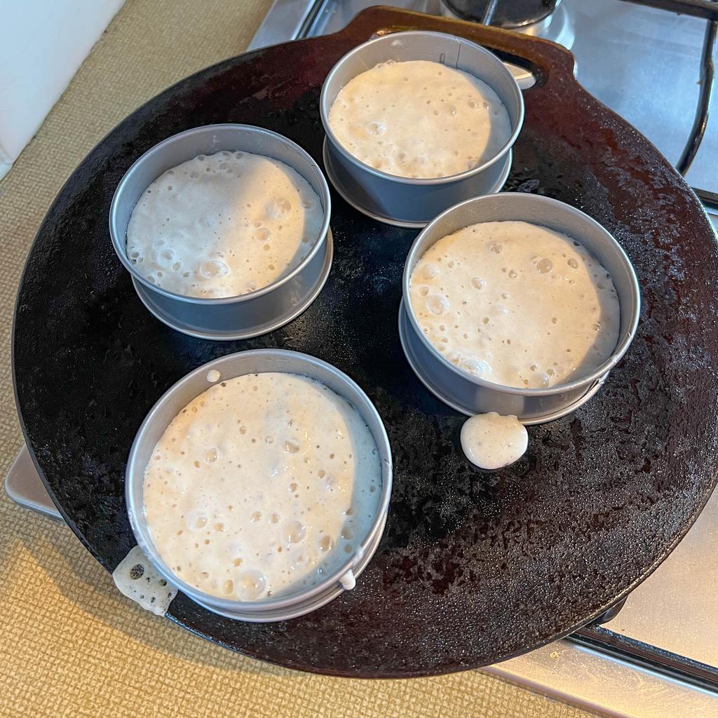 Sourdough crumpets in metal rings on the bake stone.