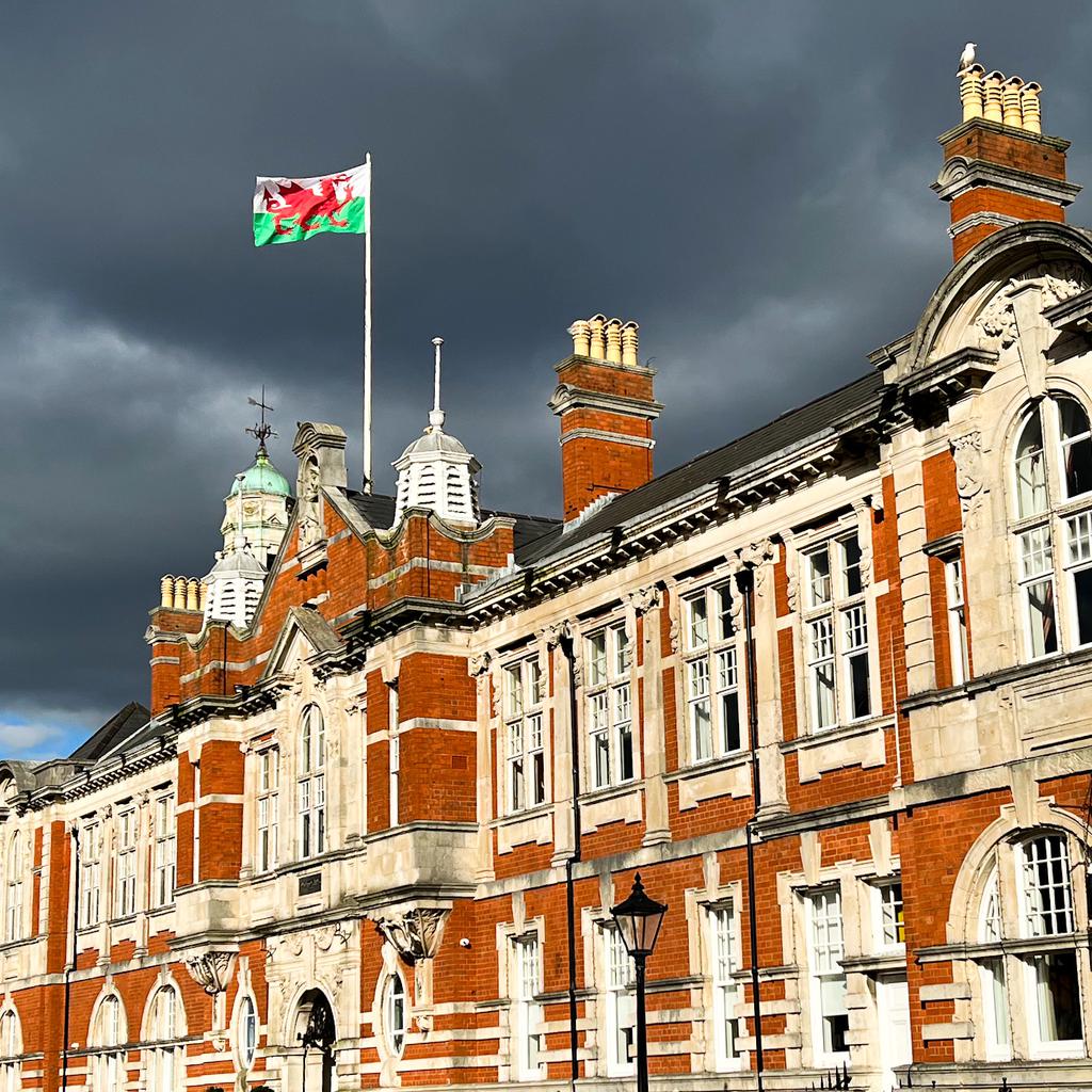 The lovely brick exterior of Morgans Hotel in bright sun with the Welsh flag in front of dark, dramatic clouds.