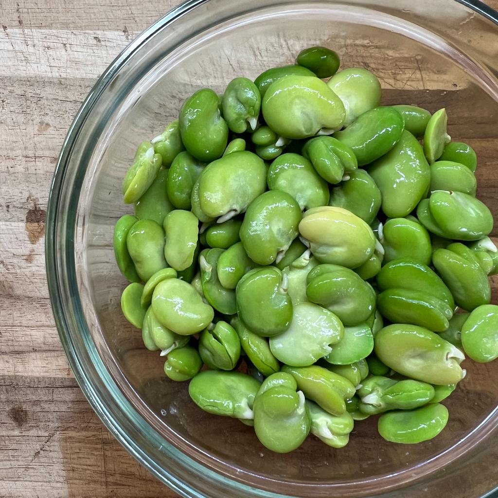 Bright green shelled broad beans in a bow.
