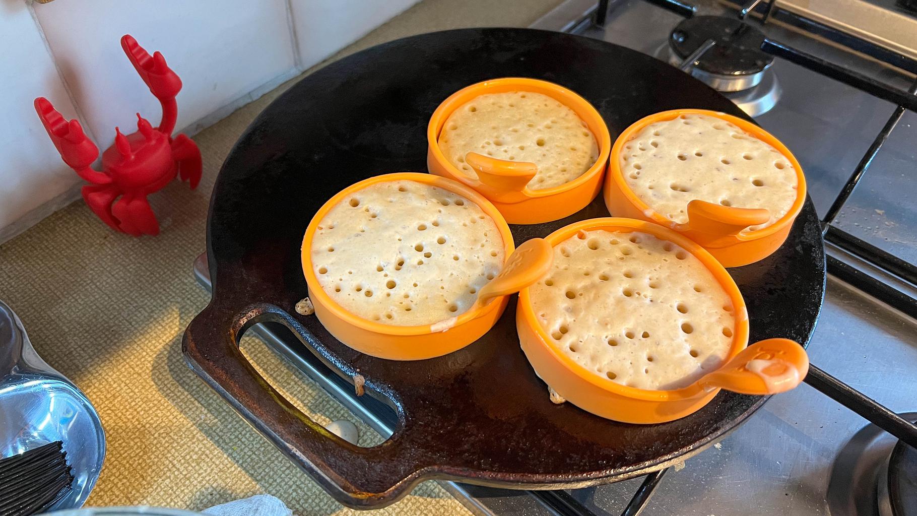 Four crumpets in rings on the bakestone. They're full of bubbles and starting to cook through to the top.