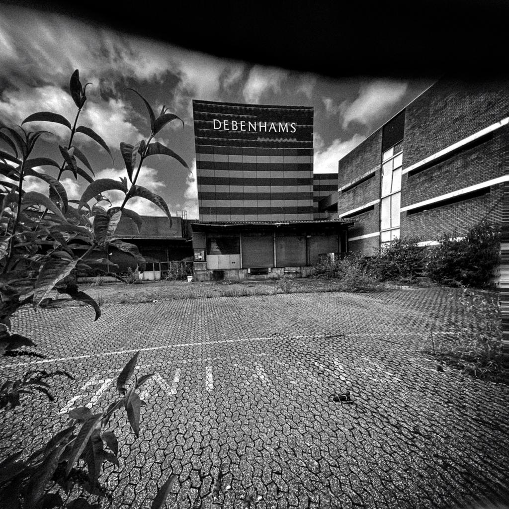 Black and white photo of Debenhams department store (now closed) across a mostly disused and slightly dilapidated lot. #PretensionsOfArt