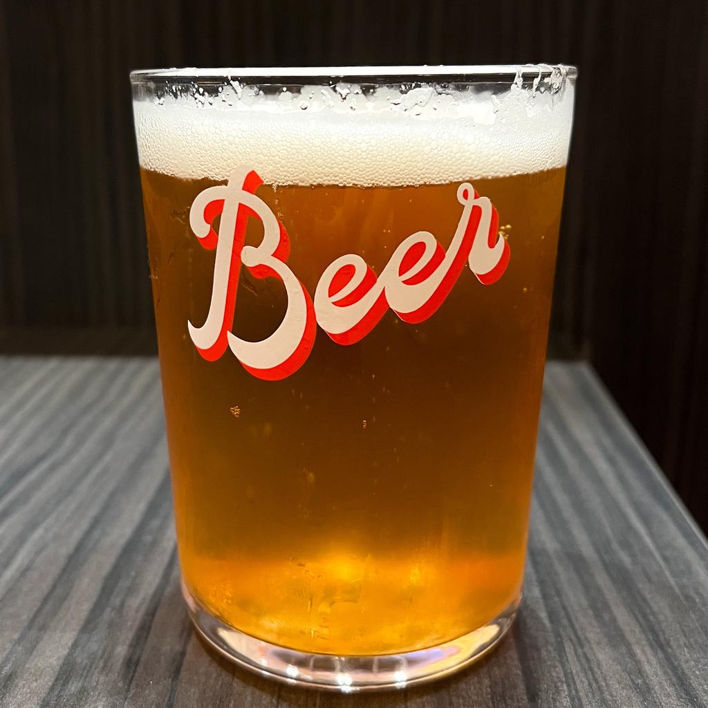 Beer in a somewhat unusually squat pint glass. The word “Beer” is written on the glass in a scriptish font.